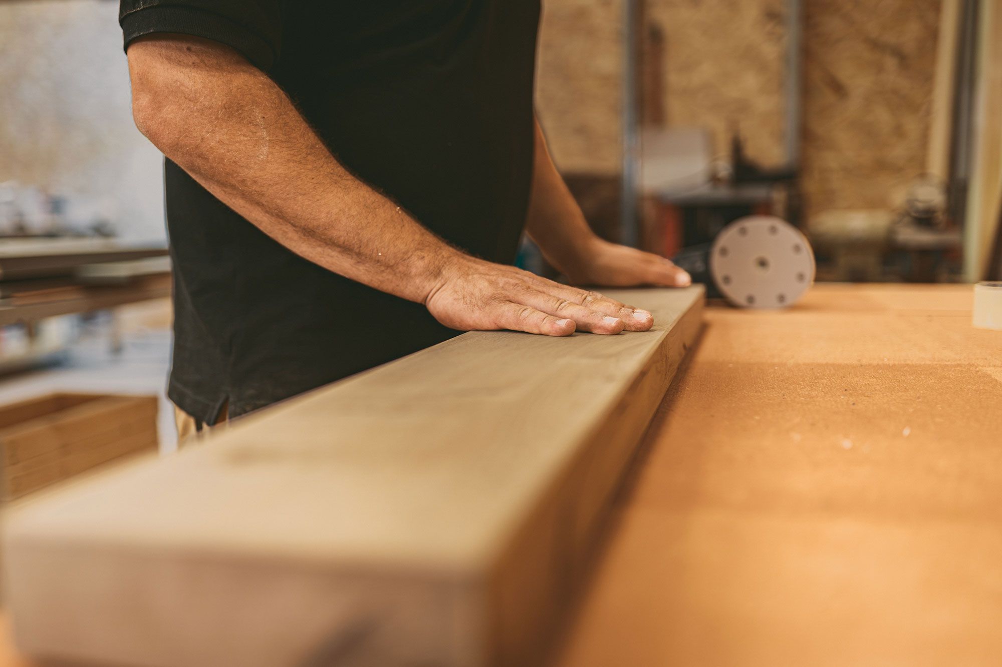 Hand prüft die Oberfläche eines Massivholzbretts in der Tischlerei